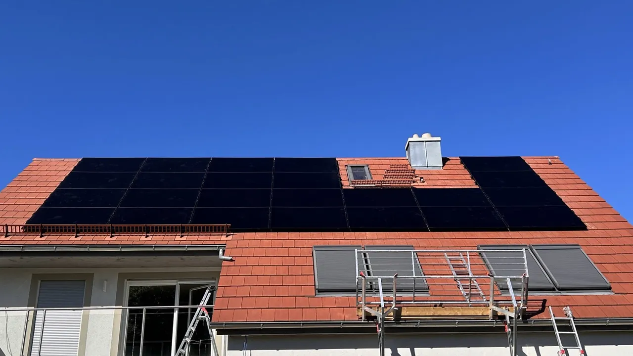 Zwei Monteure setzen auf einem Ziegeldach das letzte Solarmodul in die Unterkonstruktion