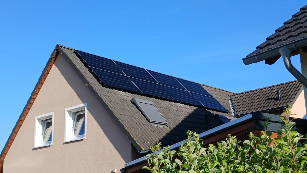 Giebelhaus mit dunklem Dach und Solarmodulen vor blauem Himmel