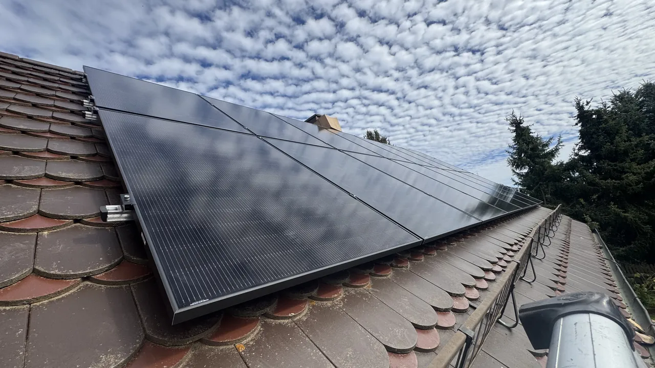 Schwarze Solarmodule auf einem Biberschwanzdach, darüber Schäfchenwolken